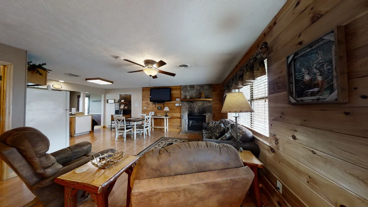 This interior image captures the main living area, with a comfortable seating arrangement, a warm gas fireplace surrounded by wooden paneling, and a glimpse of the adjoining dining area. The layout encourages communal gatherings, and the cozy ambiance is perfect for fireside relaxation or movie nights.