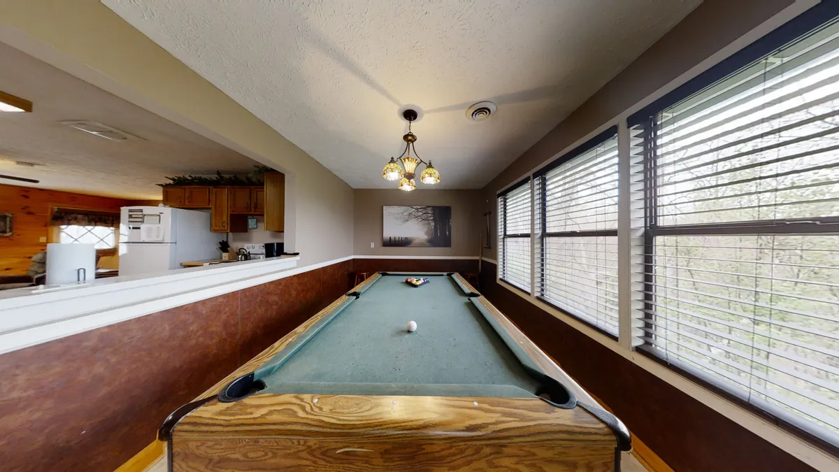 A spacious game nook is the focal point here, featuring a pool table beneath a rustic chandelier and surrounded by windows that invite natural light. The setup is ideal for friendly competition and socializing, with enough space for everyone to participate or spectate.
