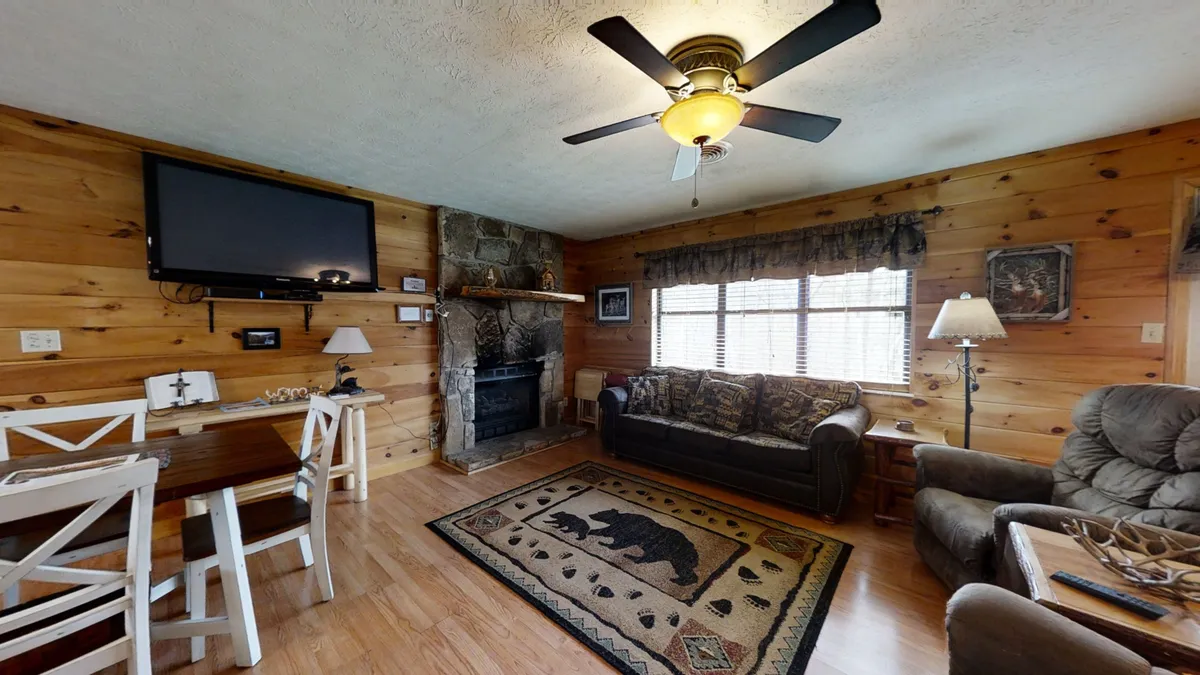 This image offers an alternate perspective of the living area, spotlighting a cozy fireplace, a comfortable couch, and a dining table on a patterned rug. The setup supports both relaxation and shared meals, illustrating the versatility of the cabin’s communal space.