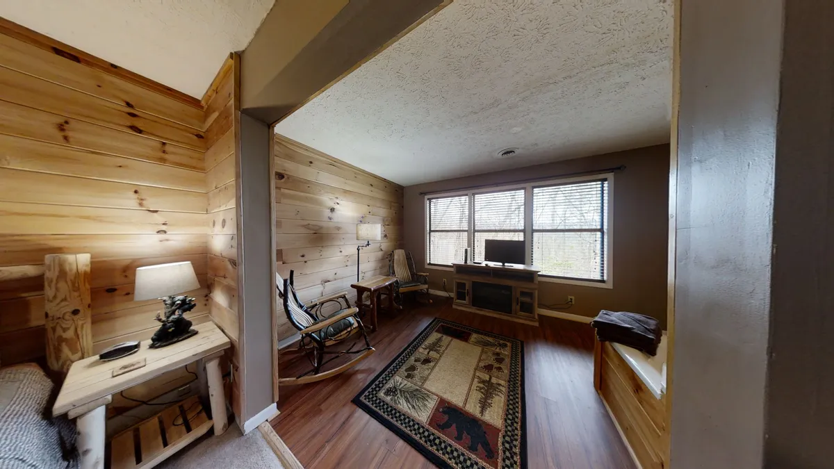 A cozy interior shot featuring classic wooden walls, large windows that offer a glimpse of the outdoors, and a traditional wooden rocking chair set on a patterned rug. Natural light streams in, evoking the peaceful connection between indoor and outdoor living.