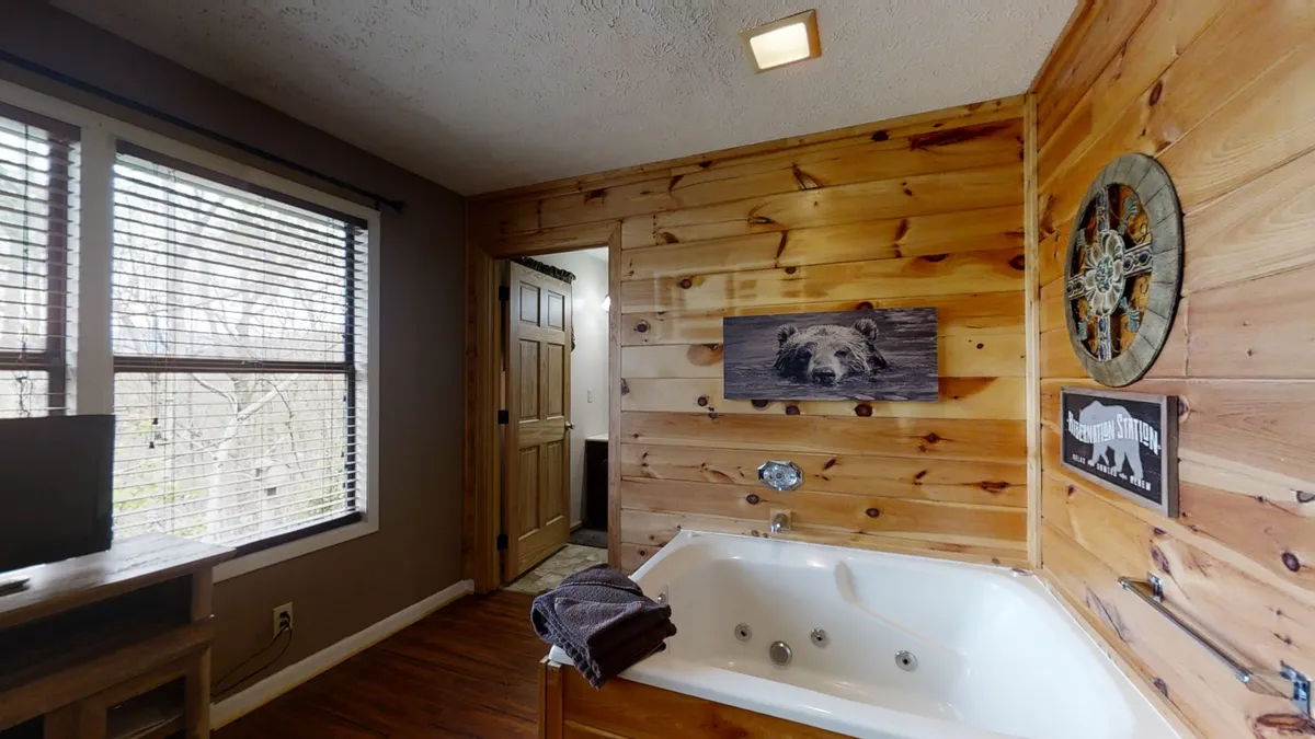 A tranquil scene with a jacuzzi tub set against wooden walls, a framed bear artwork, and a decorative wall clock. The space feels intimate, perfect for relaxing soaks and self-care, with an emphasis on comfort and privacy.