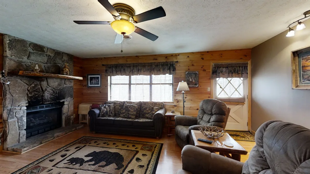 A cozy living room centers around a beautiful stone fireplace, with a plush, bear-patterned sofa inviting guests to unwind. The wooden coffee table and rustic décor create a warm and inviting atmosphere, ideal for relaxing or gathering for a group movie night.