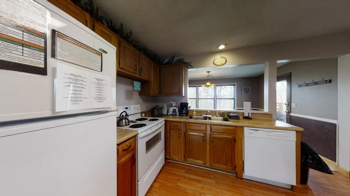 The image draws attention to the kitchen’s modern appliances, wooden cabinetry, and an inviting window view, emphasizing functionality and warmth. The countertop appears ready for meal prep, and the light from the window adds an airy feel to the space.