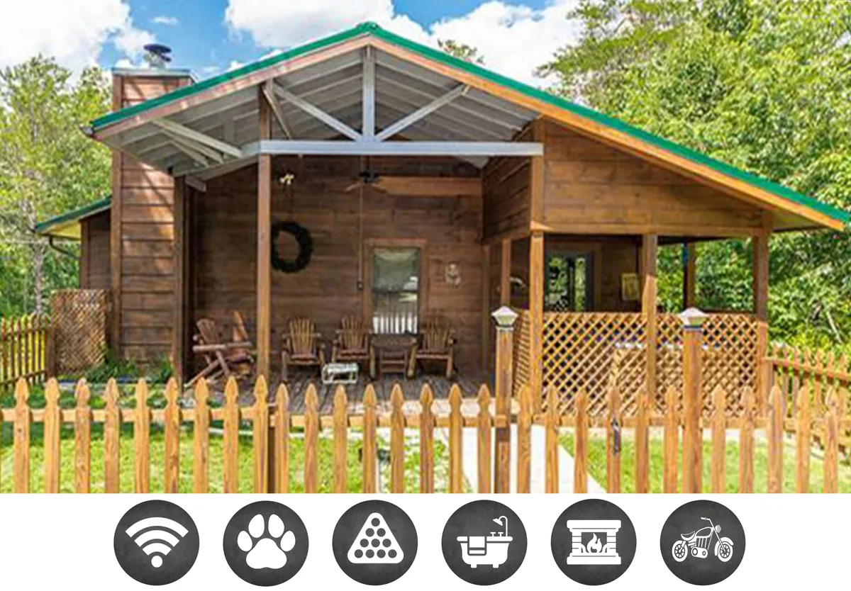 The image shows the exterior of a cozy wooden cabin with inviting porch chairs, a decorative wreath on the front door, and a fenced-in yard. The porch looks out onto a scenic view, perfect for relaxing at sunset or enjoying morning coffee amidst the peaceful natural surroundings.